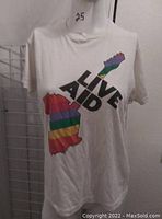 Front view of white T-shirt with a rainbow striped guitar graphic and 'LIVE AID' text