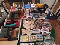 Overview of assorted vintage model train cars, boxes of tracks, train-themed apparel, and various small accessories and collectibles spread on a green surface.
