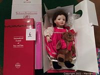 Porcelain doll Natasha in original white box with red Ashton Drake Galleries box and literature on green surface.