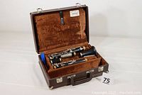 Opened hard brown case with plush brown interior showing disassembled clarinet sections and mouthpiece inside.