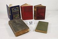 Five antiquarian books arranged with visible covers showing various colors and wear