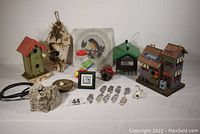 Photo showing all bird-related items including birdhouses, feeders, carved birds, plaques, and a framed picture, laid out on a table.