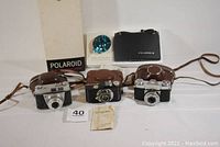 All four cameras shown together with cases, Polaroid with box and manuals, cameras front view