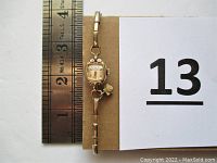 View of entire ladies wristwatch alongside ruler to show size approximately 1.5 inches in case diameter and 2.5 inches band diameter.