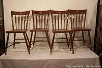 Full view of four matching brown painted farm-style wooden chairs with flower decals on backrest.