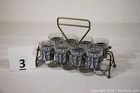 Overall shot of eight shot glasses in original steel rack with handle.