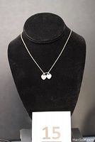 Necklace displayed on black stand showing two heart pendants on a thin silver chain.