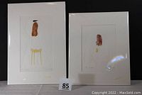 Two matted art prints by Lika Tov side-by-side on a surface, showing full mats and print artwork inside them, with lot number in front