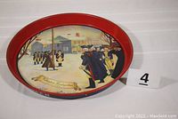 Full view of the round metal tray showing the painted historical scene and red rim.