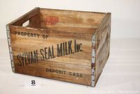 Full view of the wooden milk bottle deposit crate showing side with printed logo and metal edge protectors.