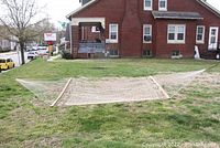Full view of the rope hammock laid out on grass showing wooden spreader bars at each end and the woven rope bed with chains attached.