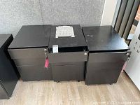 Front view of three black metal file cabinets side by side, each with keys and three drawers.