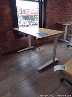 Front left perspective of desk showing bamboo top, white legs and control cable