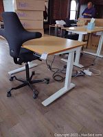 Wide view of Jarvis desk with bamboo top and white base alongside HAG ergonomic chair