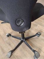 Lower portion of HÅG office chair showing black fabric upholstery, tilt adjustment knob and five-star base with foot-shaped pads