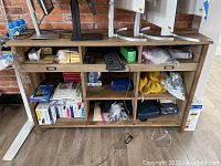 Front view of wooden office shelf filled with office supplies and computer monitors on top.
