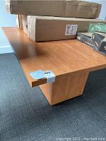 Photo showing the light natural maple finish and edge of the square office table with boxes placed on top.