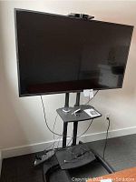 Front view of Sony TV mounted on mobile stand with top shelf and cables