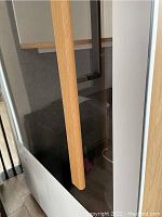 Exterior view of glass door with oak-tone wooden vertical handle and black metal frame on white panel