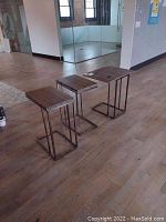 Three nesting work tables arranged side by side on wood floor in open position