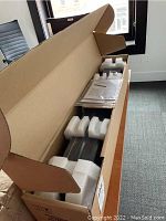 Open cardboard box showing foam inserts, plastic-wrapped sound bar housing, and manuals