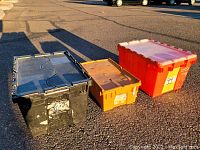 Three plastic storage bins with lids on pavement, colors black, orange, and red. Showing front and side angles of bins.