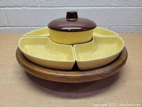 Top-down photo showing the yellow speckled ceramic serving dishes and brown lidded dip bowl on wooden lazy Susan base.