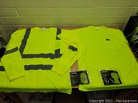 Two long sleeve high visibility work shirts laid flat on a surface, one with reflective gray striping, the other plain bright yellow, both new in XL and M sizes.