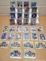 Front view of multiple vintage baseball cards arranged on a table, displayed upright on a white stand and laid flat. Cards show players with team names such as Orioles, Expos, and Cardinals.
