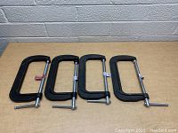 Four black cast iron 8 inch Bessey C clamps laid flat on a wooden surface showing the frames and screws