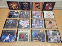Lot of 16 CDs displayed in rows on a table showing front covers including Guns N' Roses, Metallica, AC/DC, Van Halen.