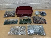 Multiple angles of glass marbles, polished decorative stones in plastic bags, and a red container tray on a table.