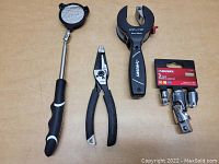 Photo of Husky telescoping mirror, wire stripper/plier, pipe cutter, and 3-piece socket adapter set on table.