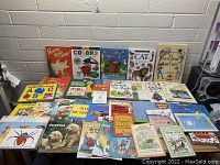 Front view of children's books arranged on a table and against a wall, showing colorful covers with a mix of educational and storybook titles.