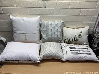 Front view of six new decorative throw pillows arranged in two rows with various patterns including plain white, geometric, botanical, and printed text designs