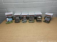 Photo showing all six River Road building collection items lined up with their original boxes behind them on a wooden surface against a light-colored wall.
