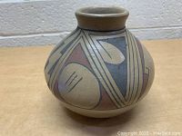 Small Native American pot with geometric painted design on beige background photographed from front angle.