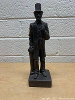 Front view of vintage Abraham Lincoln statue dressed formally, holding a document, on rectangular base against a brick wall background.