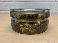 Side view of the round glass ashtray showing the gold band with embossed Fabbri name and lemon motifs on textured background.