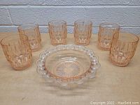 Photo showing six pink textured glass drinking glasses arranged around one pink glass dish with scalloped edge and sunburst pattern on the bottom.