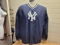 Front view of the navy blue New York Yankees pullover jacket showing large white embroidered NY logo on chest and V-neck collar with striped trim.