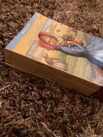 Stack of six American Girl Kirsten books with titles visible on spines and cover of Meet Kirsten facing up, showing illustrated cover of Kirsten holding rabbits.