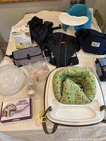 Complete set of baby gear items including carriers, jumper, chairs, and feeding accessories displayed on a bed