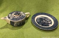 Photo showing the blue and white sailboat-shaped teapot and matching decorative plate on green fabric background.