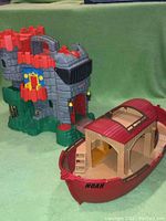 Front angle view of Fisher-Price castle playset with multiple levels, red crenellations, and interior rooms, next to Playmobil Noah's Ark toy boat in red and tan.