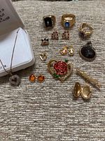 Overall view of gold plated and costume jewelry including rings, earrings, pendant, locket, and pin bar on fabric background