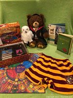 Wide view of entire lot showing Harry Potter trivia game components, Build-A-Bear bear, white owl plush, books, and Gryffindor shorts arranged on green cloth