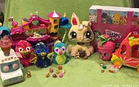 Full view of all toys showing Littlest Pet Shop amusement park, Hatchimals plush toys, Shopkins plush and vehicle, and small Squinkies figures