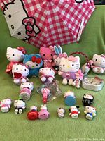 Hello Kitty plush toys, small figures, umbrella, clock, and earmuffs arranged on green surface