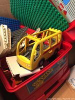 Yellow Lego Duplo bus vehicle on top of red storage tray with building blocks and baseplates